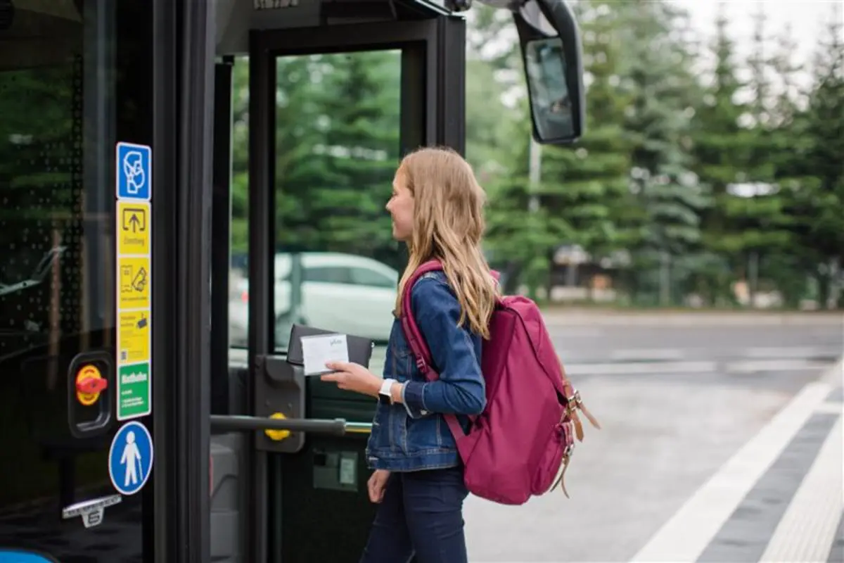 Eine Schülerin steigt in einen Bus ein und zeigt ihr Ticket vor. 