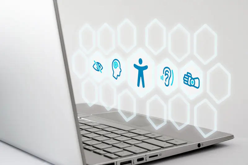 Das Bild zeigt einen Laptop. Im Bildzentrum sind die Symbole für Sehbehinderung, kognitive Behinderung, Hörbehinderung und motorische Behinderung abgebildet. 