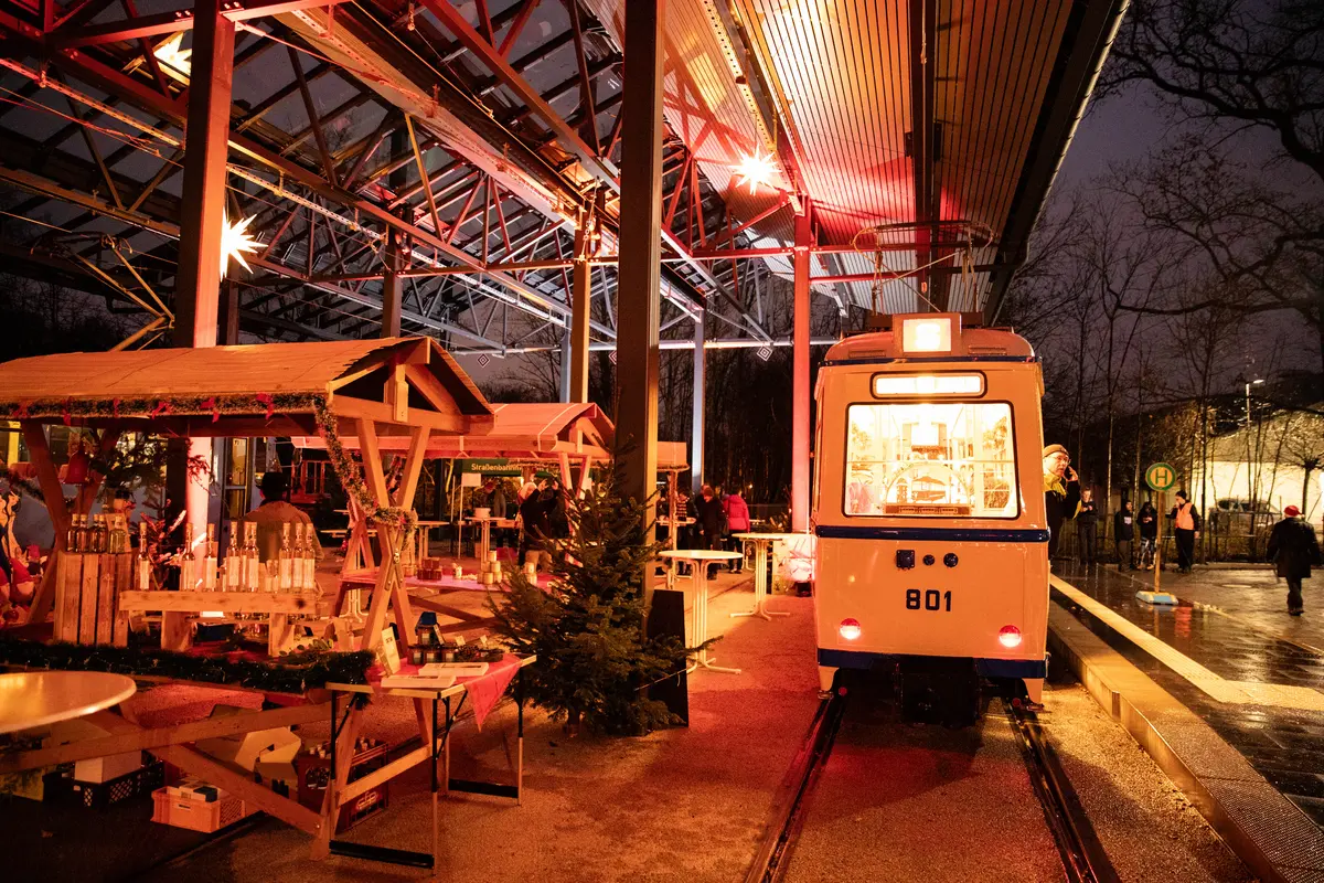 Neben weihnachtlichen Ständen steht eine historische Straßenbahn. Es ist dunkel und alles ich weihnachtlich beleuchtet.