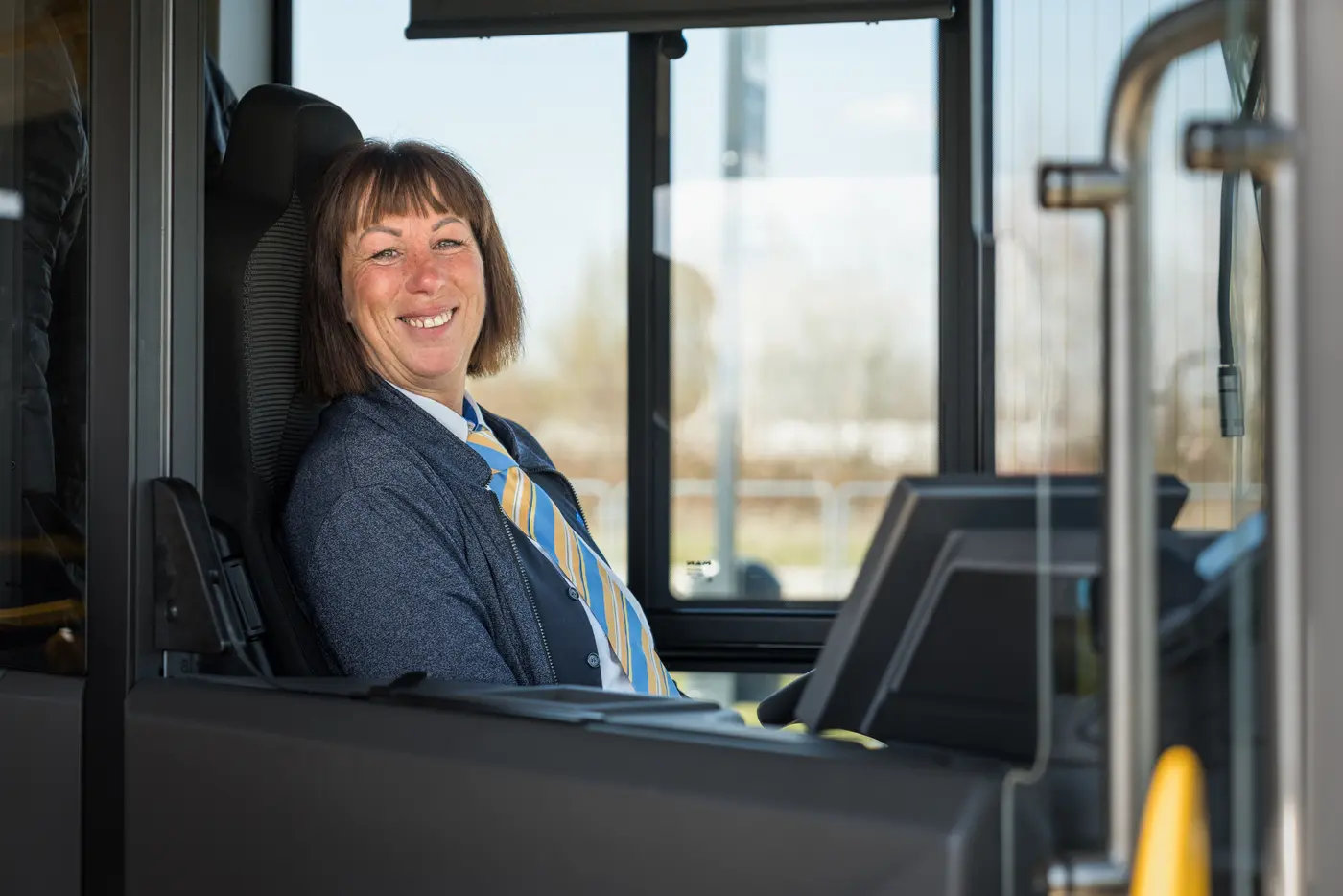 Eine Busfahrerin sitzt in der Fahrerkabine des Busses und lächelt freundlich in die Kamera
