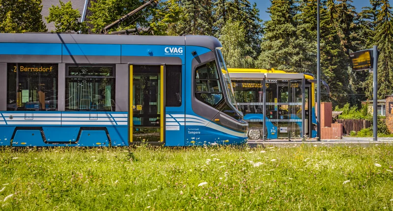 Eine Bahn und ein Bus der CVAG stehen versetzt an einer Haltestelle. Die Bahn steht vor dem Bus. Man erkennt nur den vorderen Teil der Bahn und des Busses.