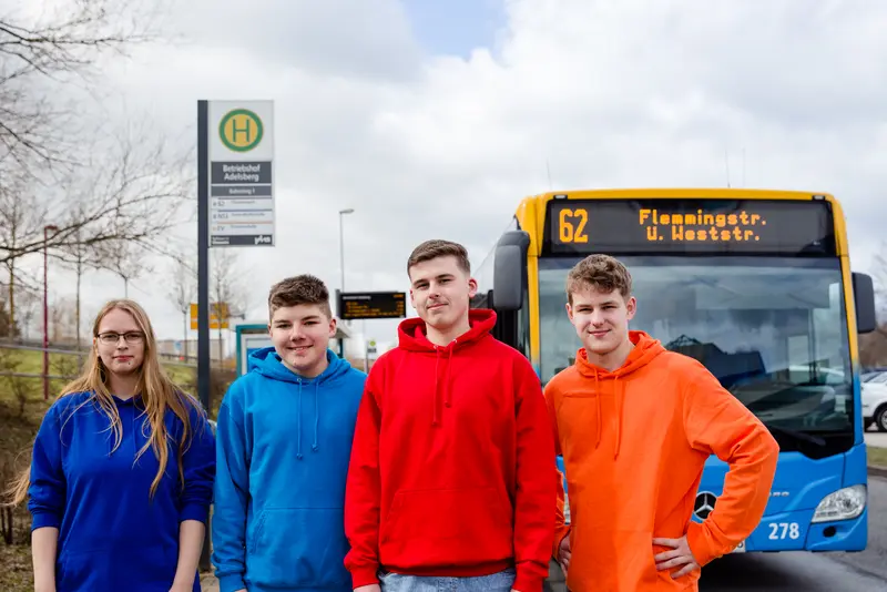 Vier Auszubildende in verschiedenfarbigen Pullis vor einem CVAG-Bus.