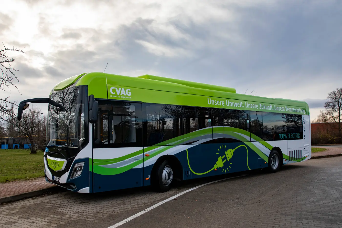 Das Bild zeigen einen Standardlinienbus der Firma Ikarus. Der Bus ist dunkelblau, weiß und grün. Auf dem Dachkranz sieht man das CVAG Logo sowie den Spruch: Unsere Umwelt. Unsere Zukunft. Unsere Verantwortung. Weiterhin steht auf dem Bus: 100% Electric. 