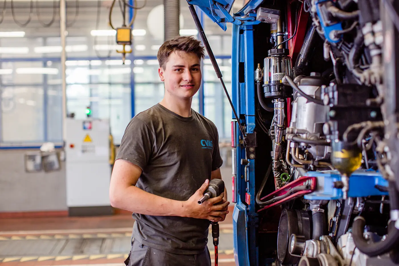 Junger Mann steht hinter der geöffneten Heckklappe eines Busse. Der junge Mann träft Werkstattkleidung mit CVAG-Logo.