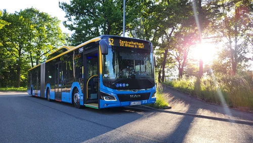 Das Bild zeigt einen CVAG Bus auf der Linie 52. Der Bus steht an einer Endhaltestelle, im Hintergrund sieht man Bäume durch die das Sonnenlicht fällt. 