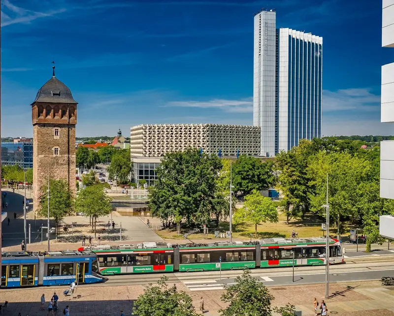 Das Bild zeigt eine Skodabahn und eine Citybahn an der Haltestelle Roter Turm. Im Hintergrund sieht man den roten Turm sowie die Stadthalle und den hohen Hotelturm.