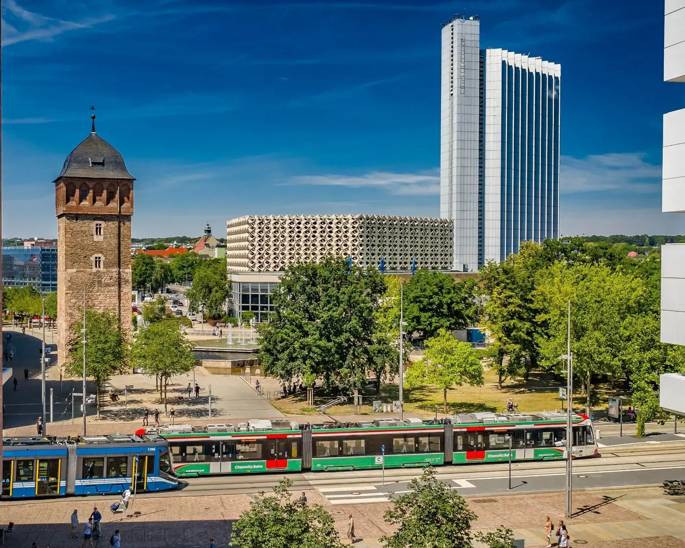Das Bild zeigt eine Skodabahn und eine Citybahn an der Haltestelle Roter Turm. Im Hintergrund sieht man den roten Turm sowie die Stadthalle und den hohen Hotelturm.