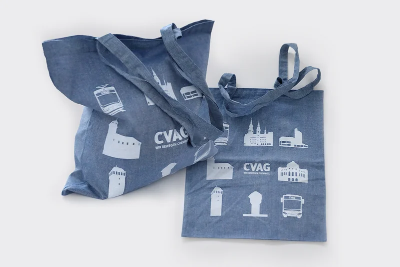A blue cotton bag featuring stylised white illustrations of Chemnitz’s landmarks. The CVAG logo is also printed in white in the centre. 