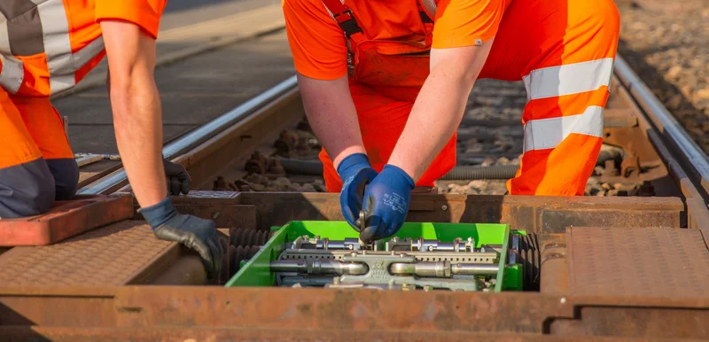 Zwei Personen in orangener Baukleidung arbeiten an einer offenen Weiche. 